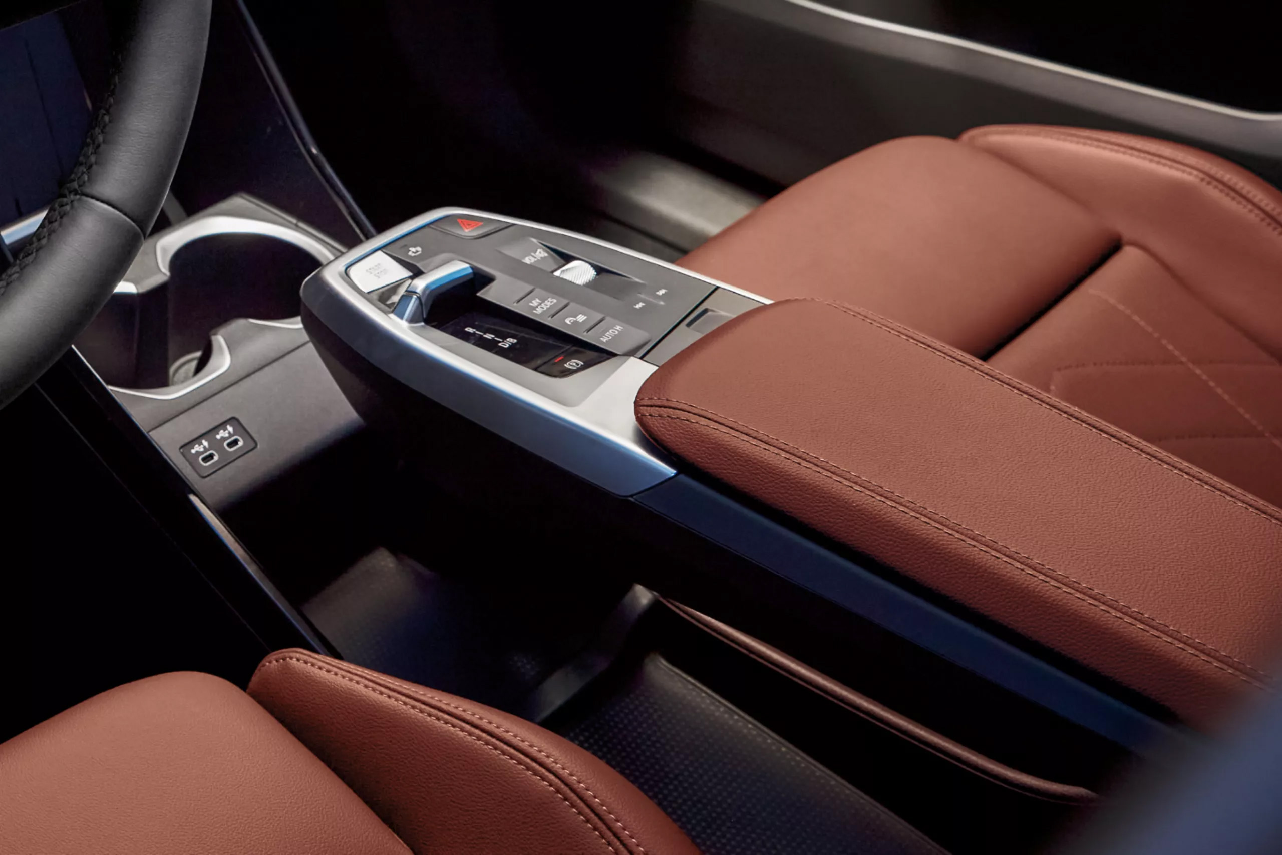 Auf dem Bild ist der moderne Innenraum eines Fahrzeugs mit einer Mittelkonsole, Bedienelementen und braunen Ledersitzen zu sehen.