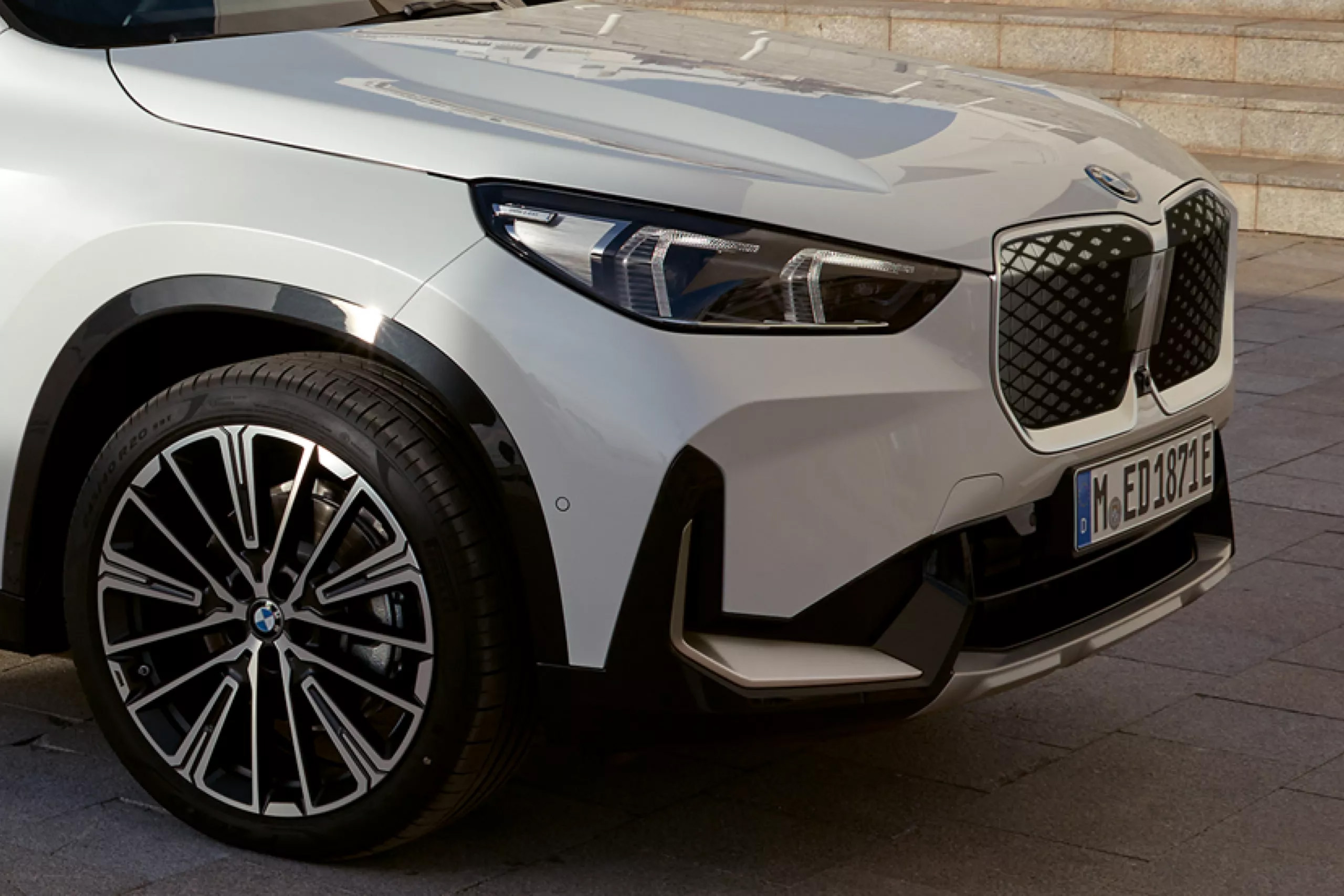 Auf diesem Bild ist die Front eines weißen BMW iX1 mit einem deutschen Kennzeichen und markanten Felgen zu sehen.