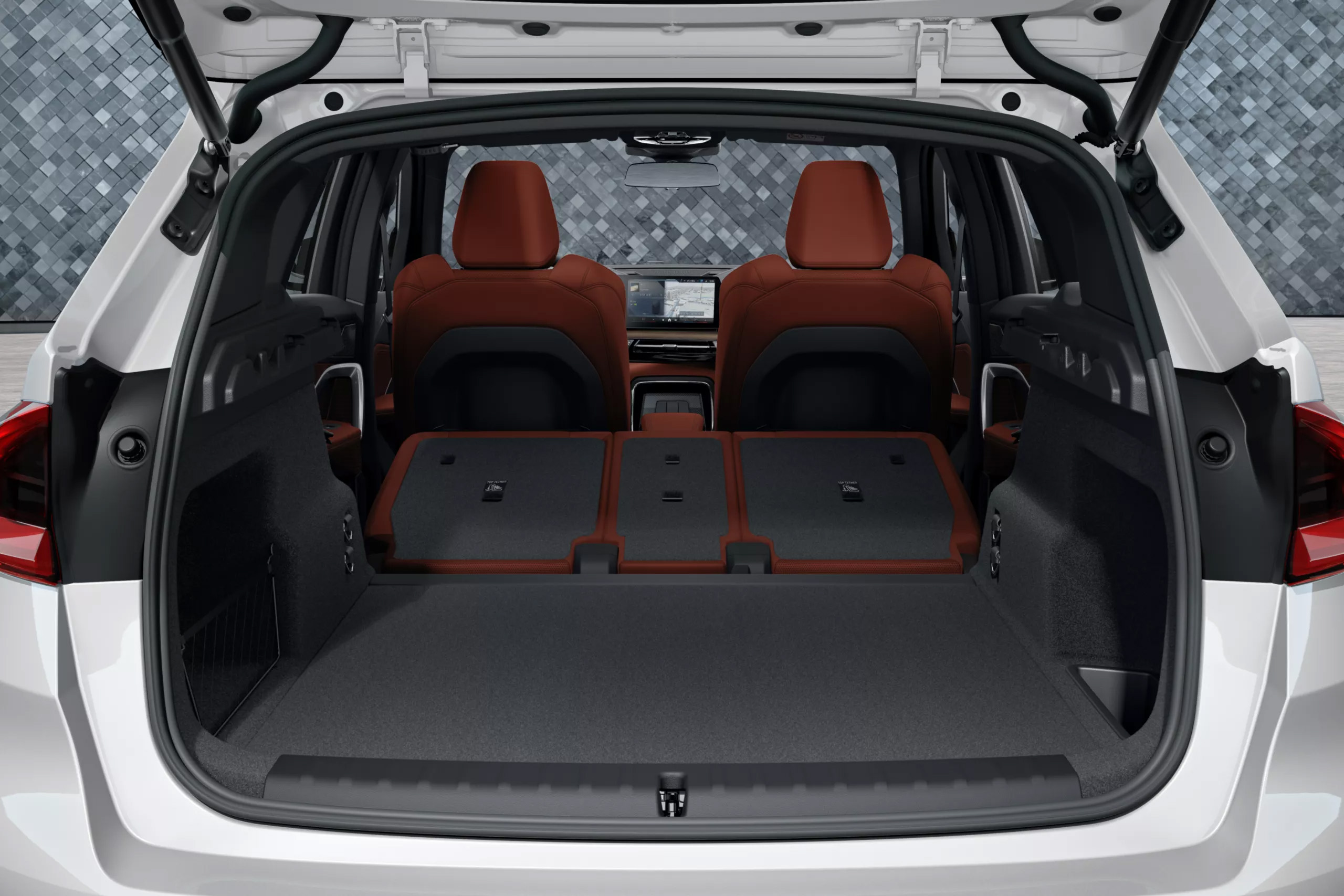 Das Bild zeigt den geöffneten Kofferraum eines modernen Autos mit umgeklappten roten Rücksitzen, die eine ebene Ladefläche bis zum vorderen Innenraum bilden.