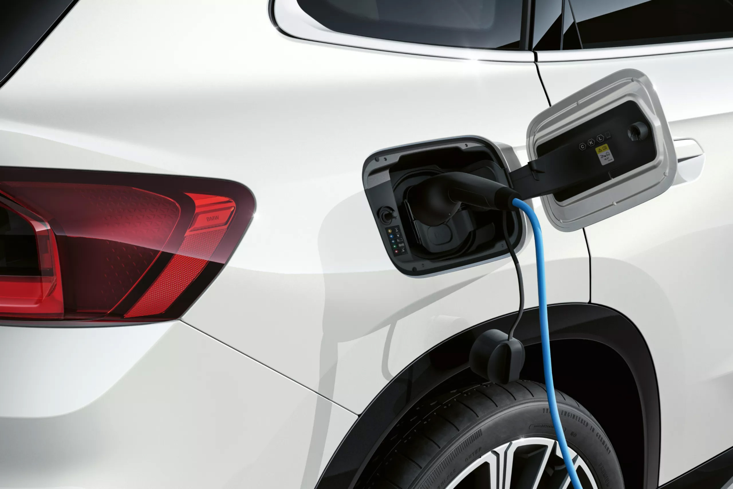 Auf dem Bild ist die Rückseite eines weißen BMW Elektroautos zu sehen, das mit einem blauen Ladekabel aufgeladen wird.