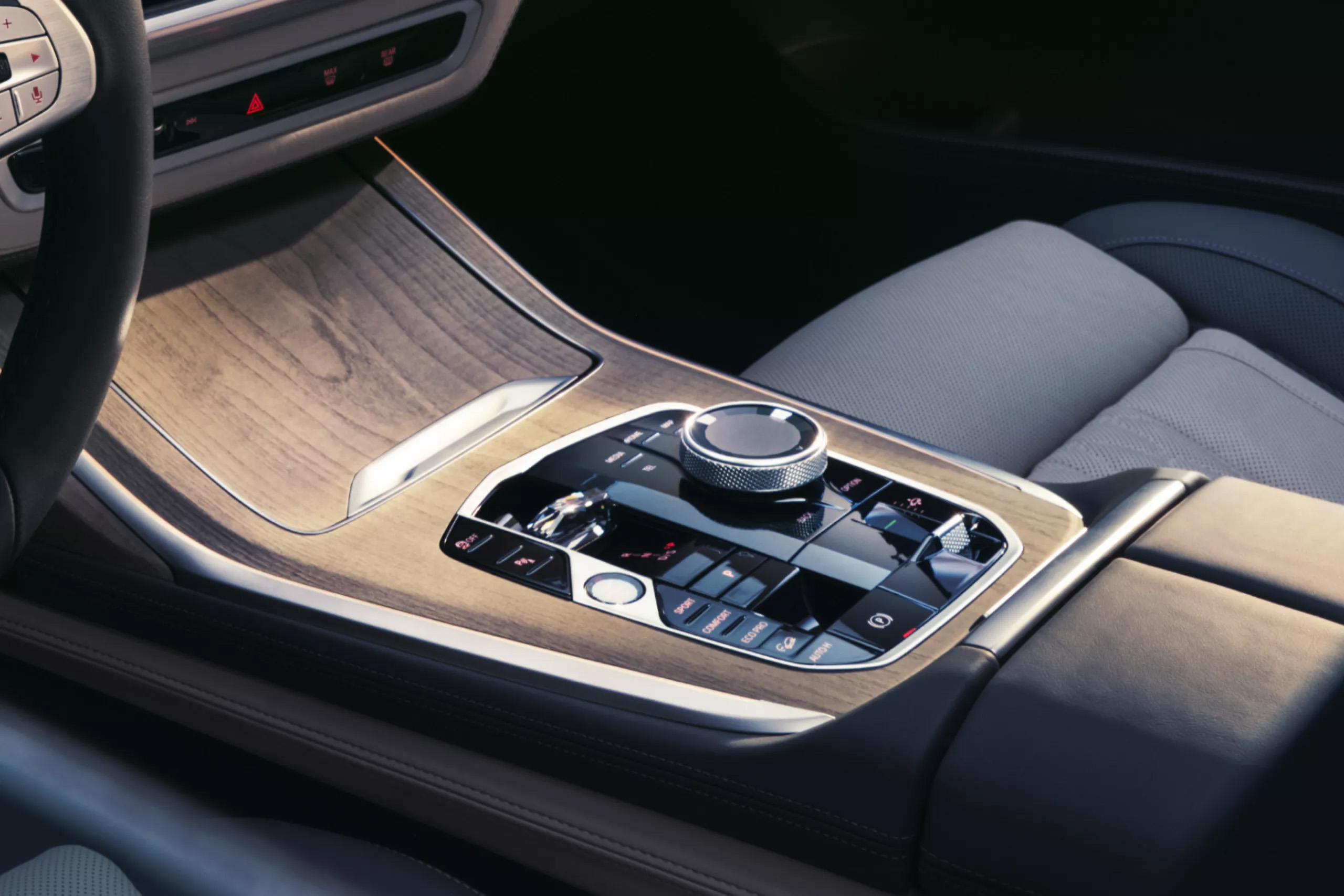 Auf diesem Bild ist der Innenraum eines Autos zu sehen, mit einem Lenkradteil, Holzzierleisten auf der Mittelkonsole, Bedienelementen und einem Autositz.